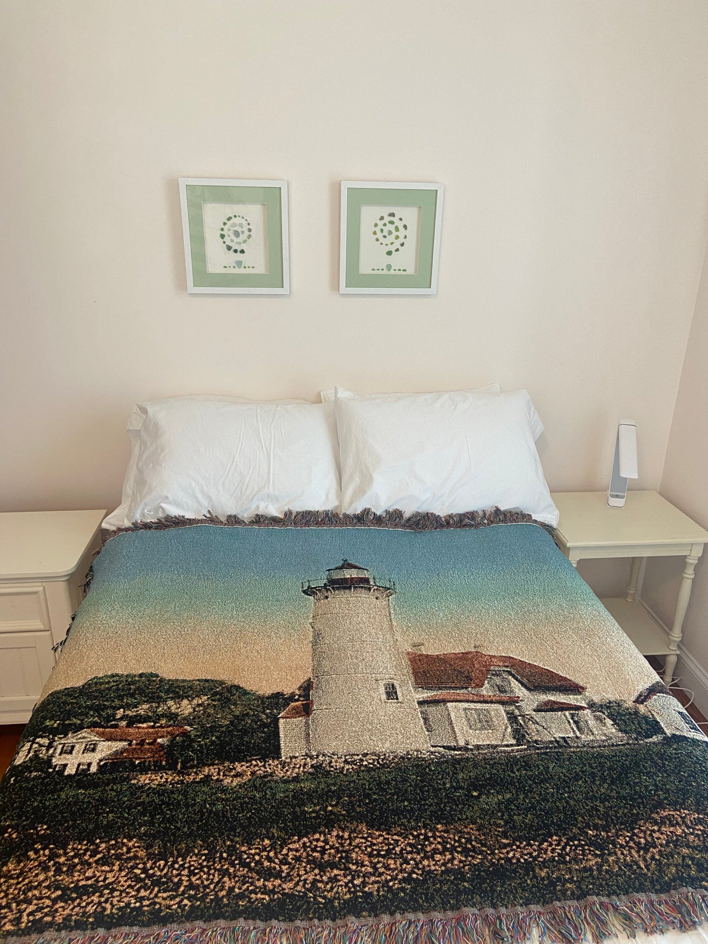 Bed with a scenic blanket featuring a lighthouse, framed pictures on the wall, and a textured rug.