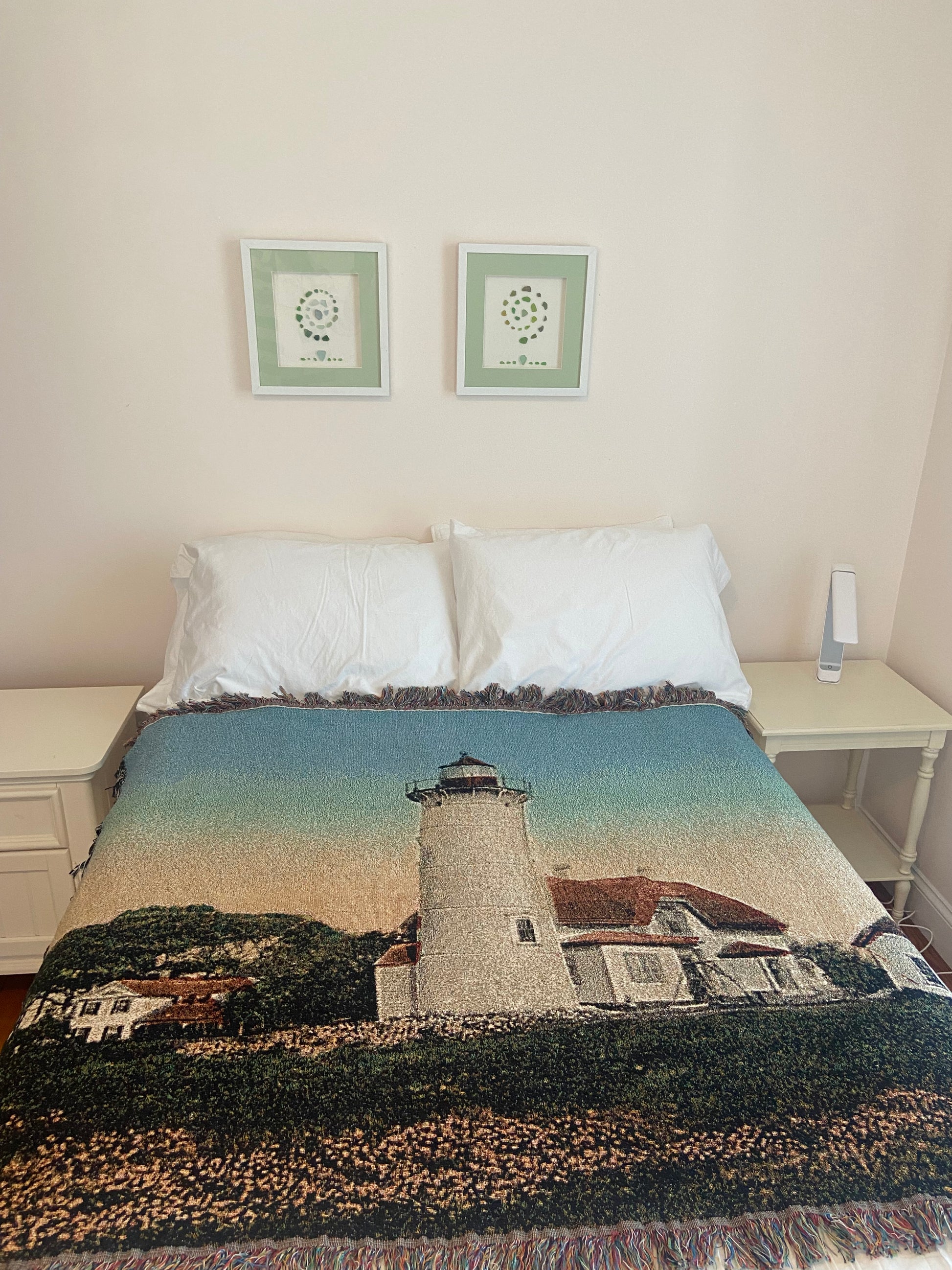 Bed with a scenic blanket featuring a lighthouse, framed pictures on the wall, and a textured rug.