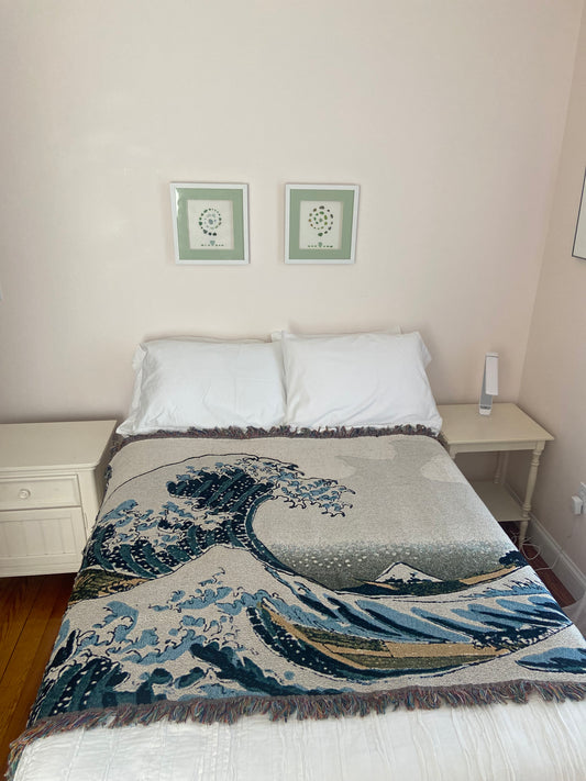 Bed with decorative blanket and pillows in a room with framed pictures on the wall.