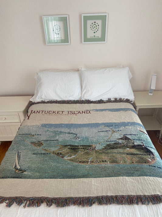 Blanket with 'Nantucket Island' text draped over a bed in a room.